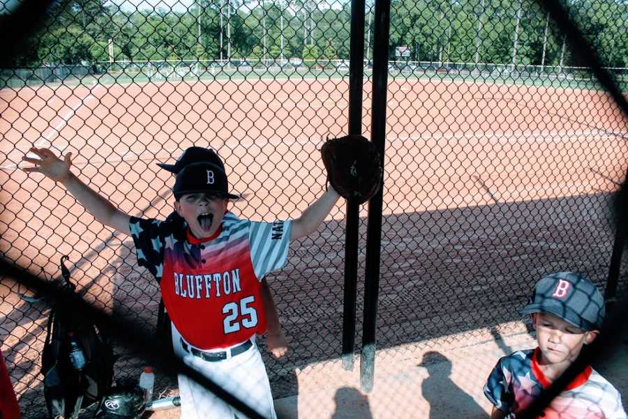 A little boy cheers from inside the dugout