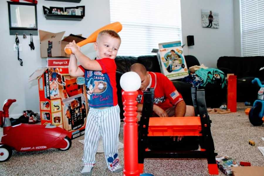 A little boy plays baseball indoors with a plastic toy bat and tee