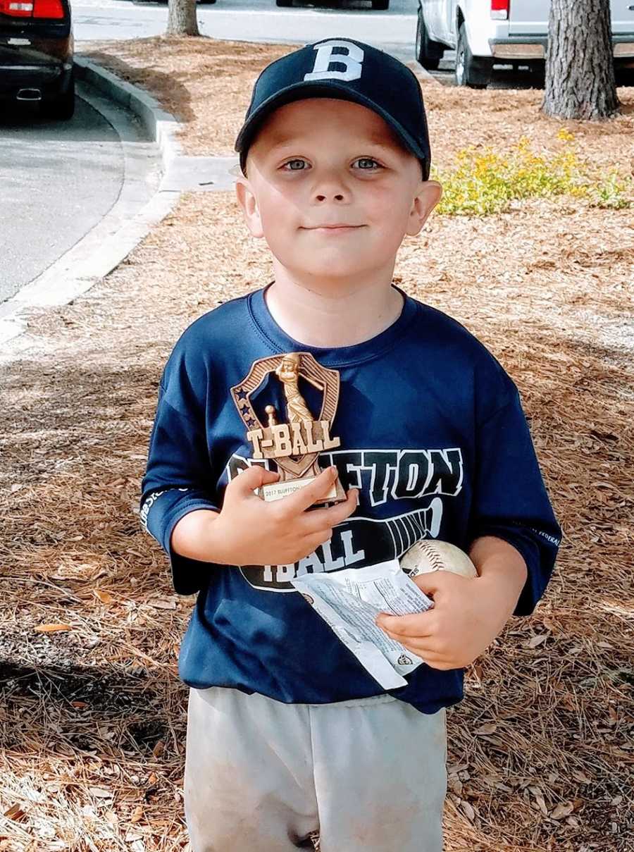 A little boy holds a t-ball trophy and a baseball