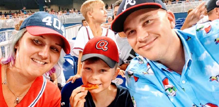 Parents sit with their son at a baseball game