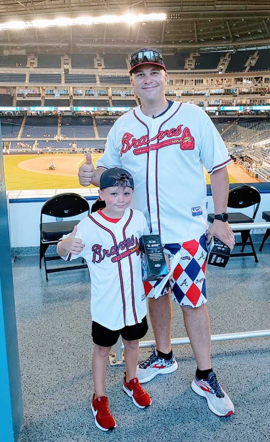 A boy and his father wearing Braves jerseys at a baseball game