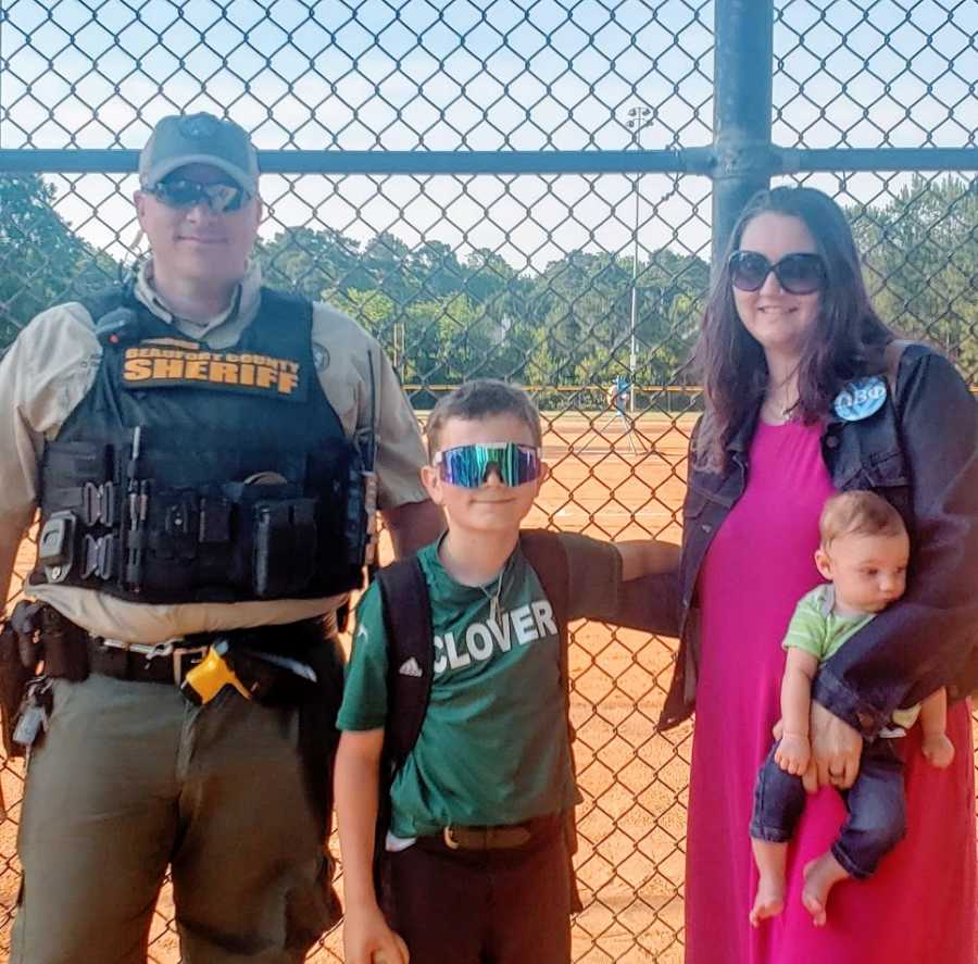 A boy stands with his parents and his little brother at a baseball field