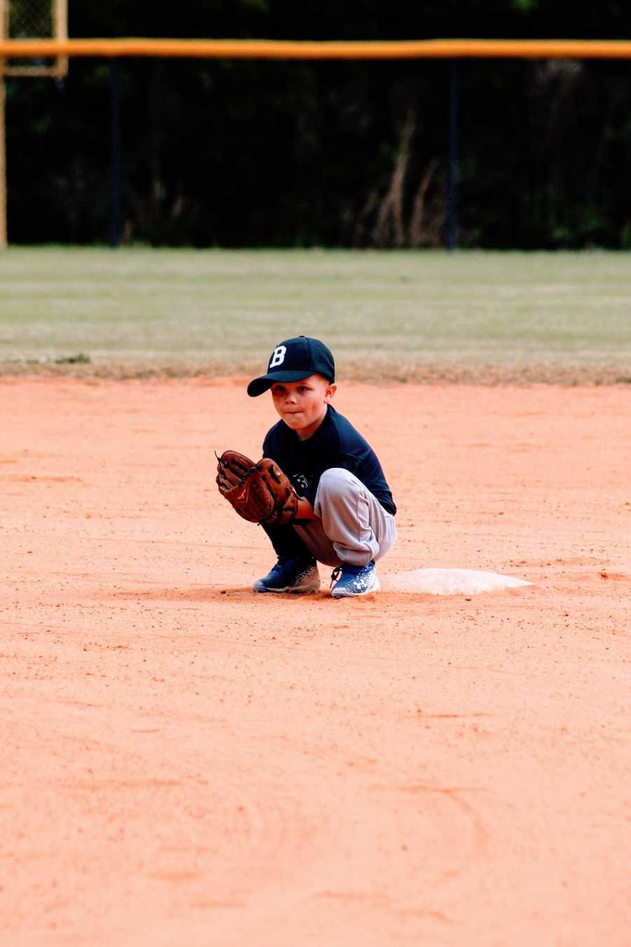 A little boy squats by the base while playing t-ball