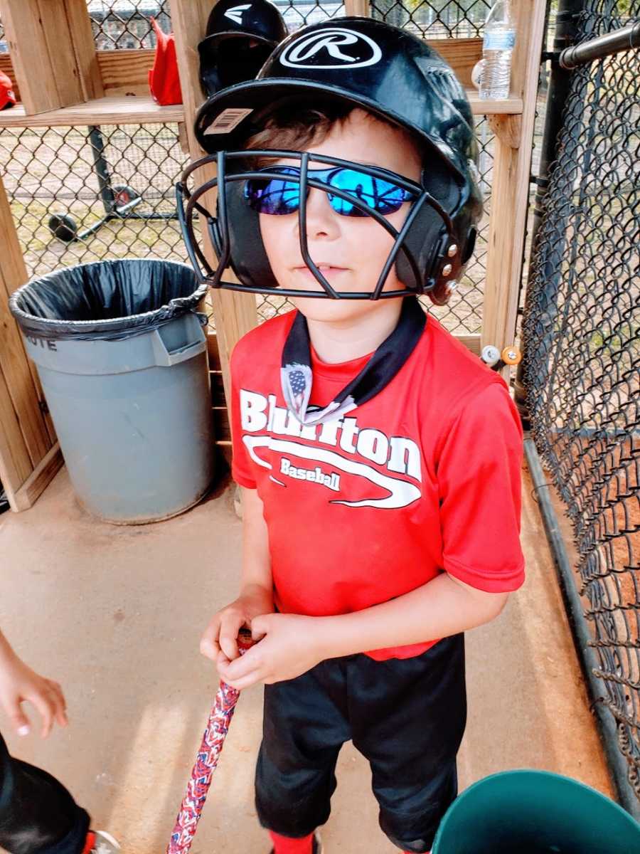 A boy wearing a batting helmet stands in a dugout