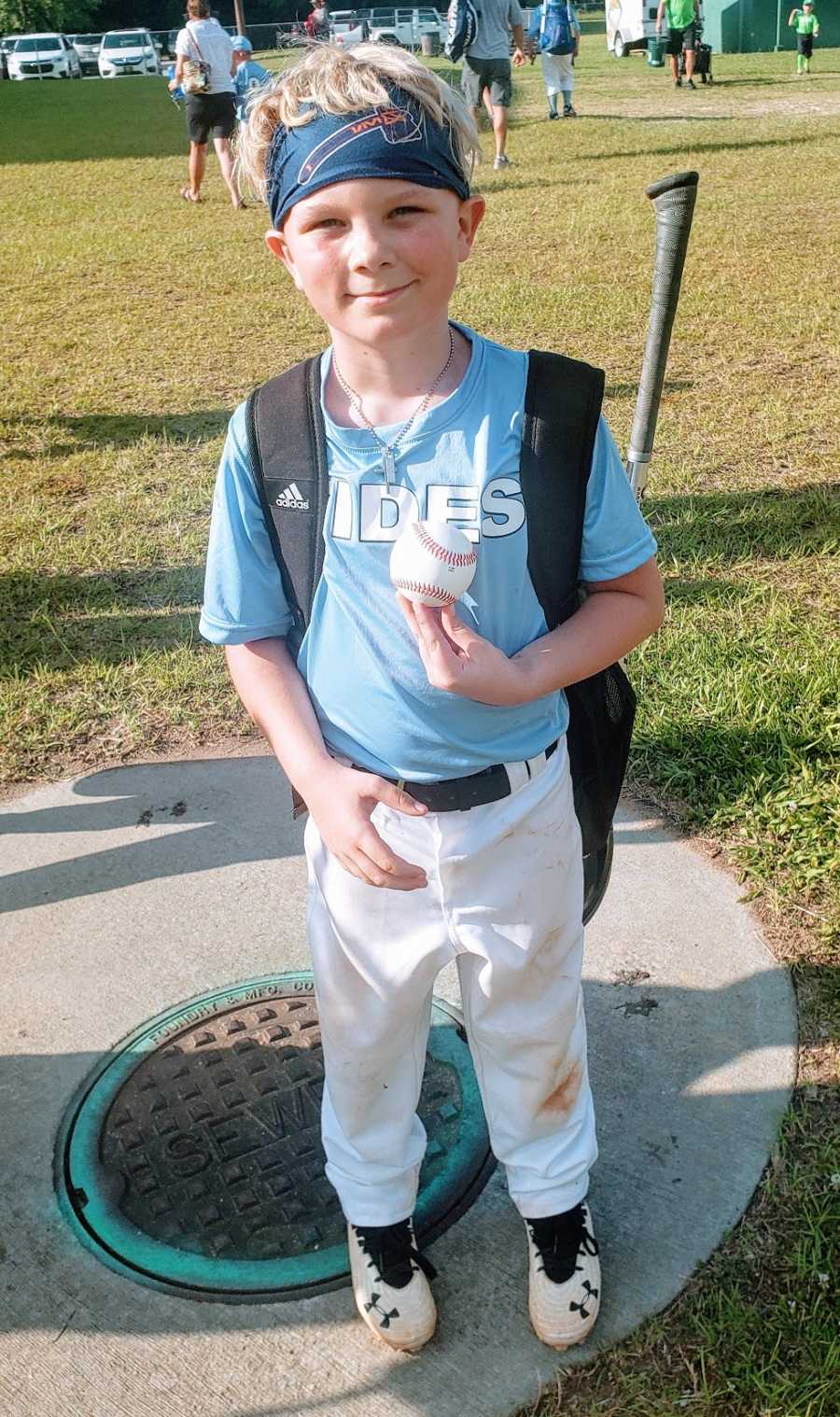 A boy holds a baseball whole wearing his baseball uniform