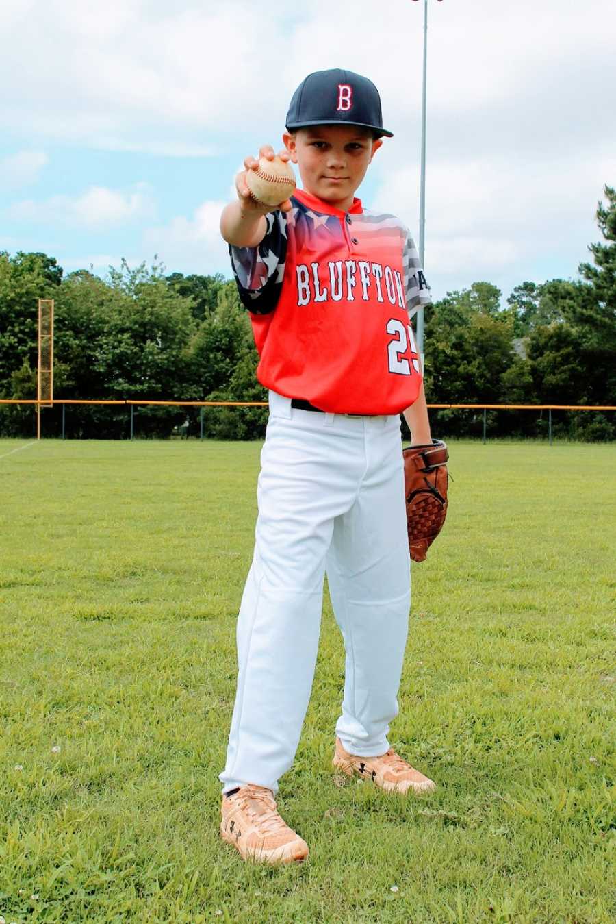 A boy wearing his all-star baseball jersey holds a baseball towards the camera