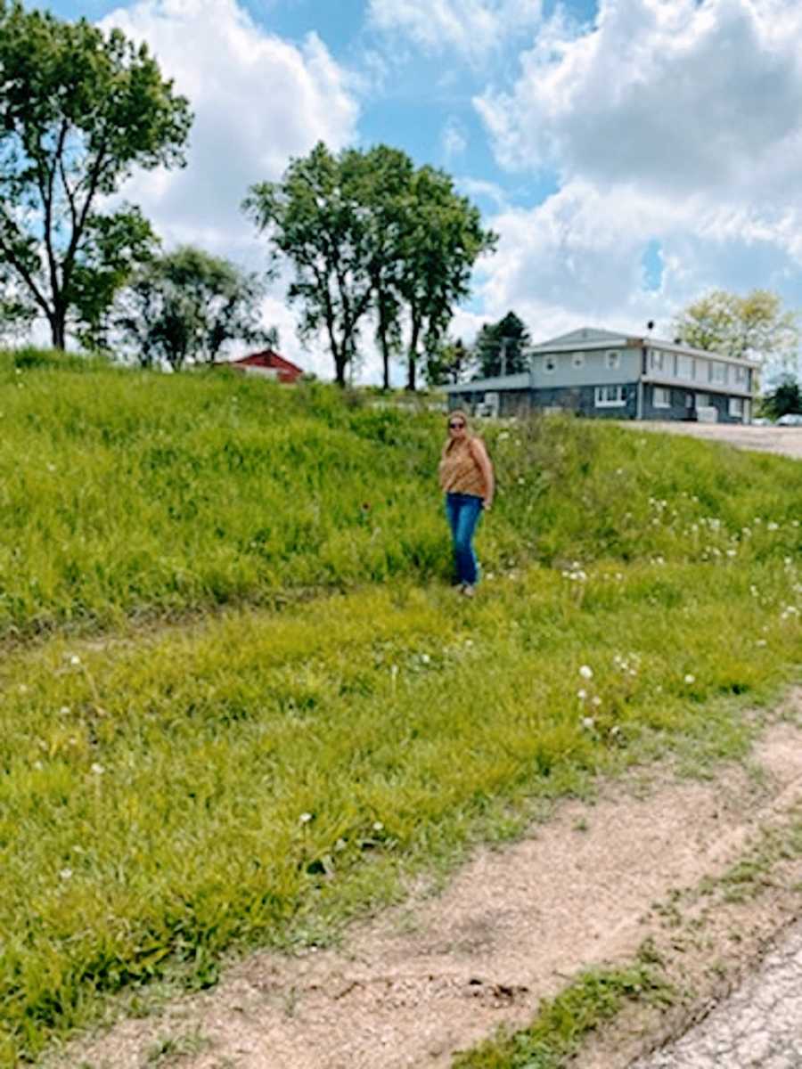 A woman stands in a field near a road