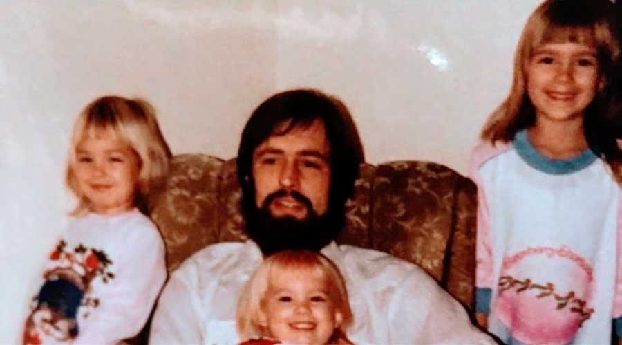 A father sits with his three young daughters