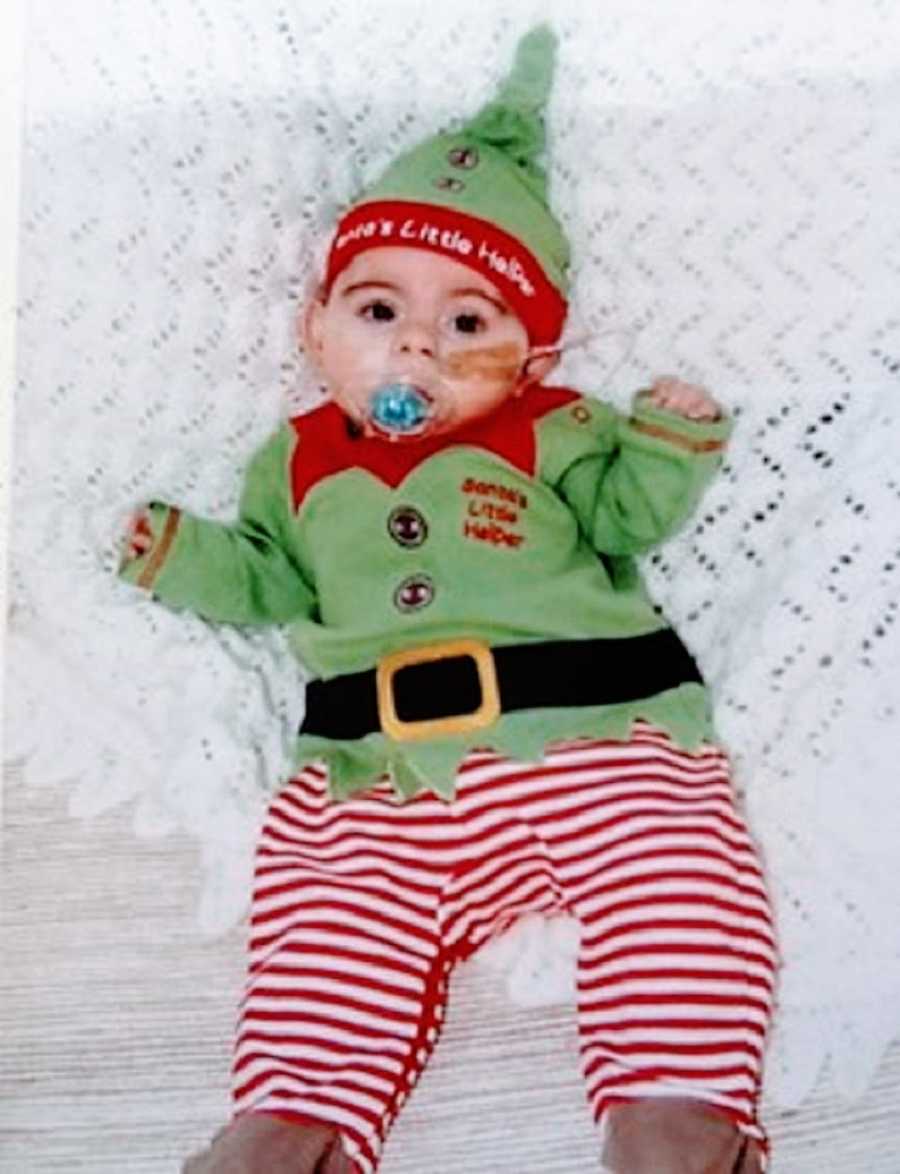 A baby girl in an elf costume lies in a crib