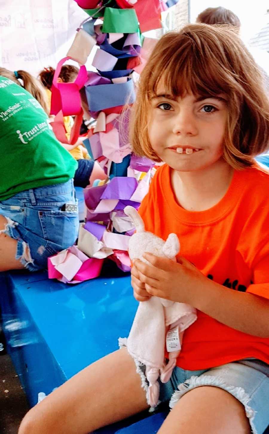 A girl wearing an orange shirt holds a soft toy