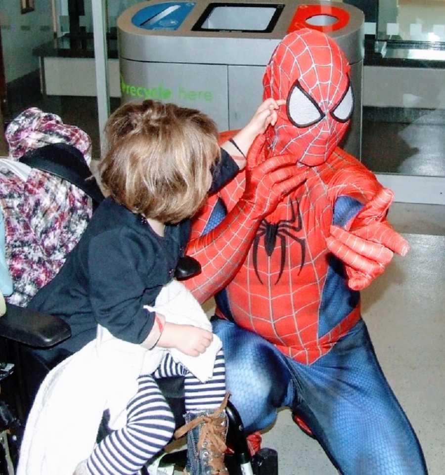 A little girl flicks at Spiderman's eye