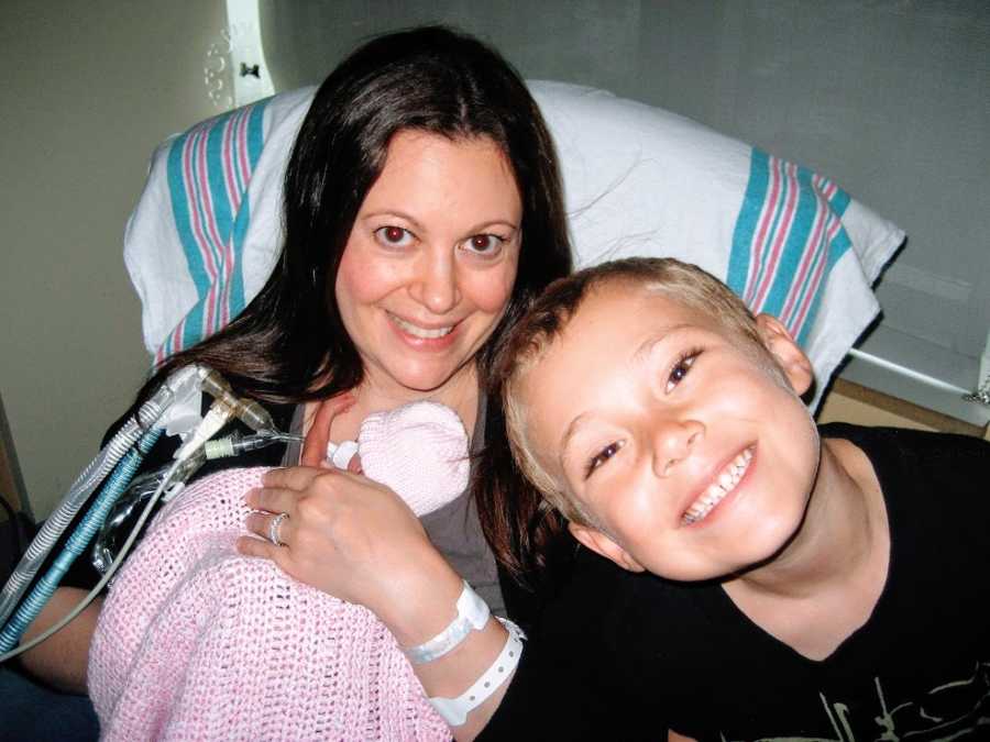 A mother holds her newborn baby girl with her son