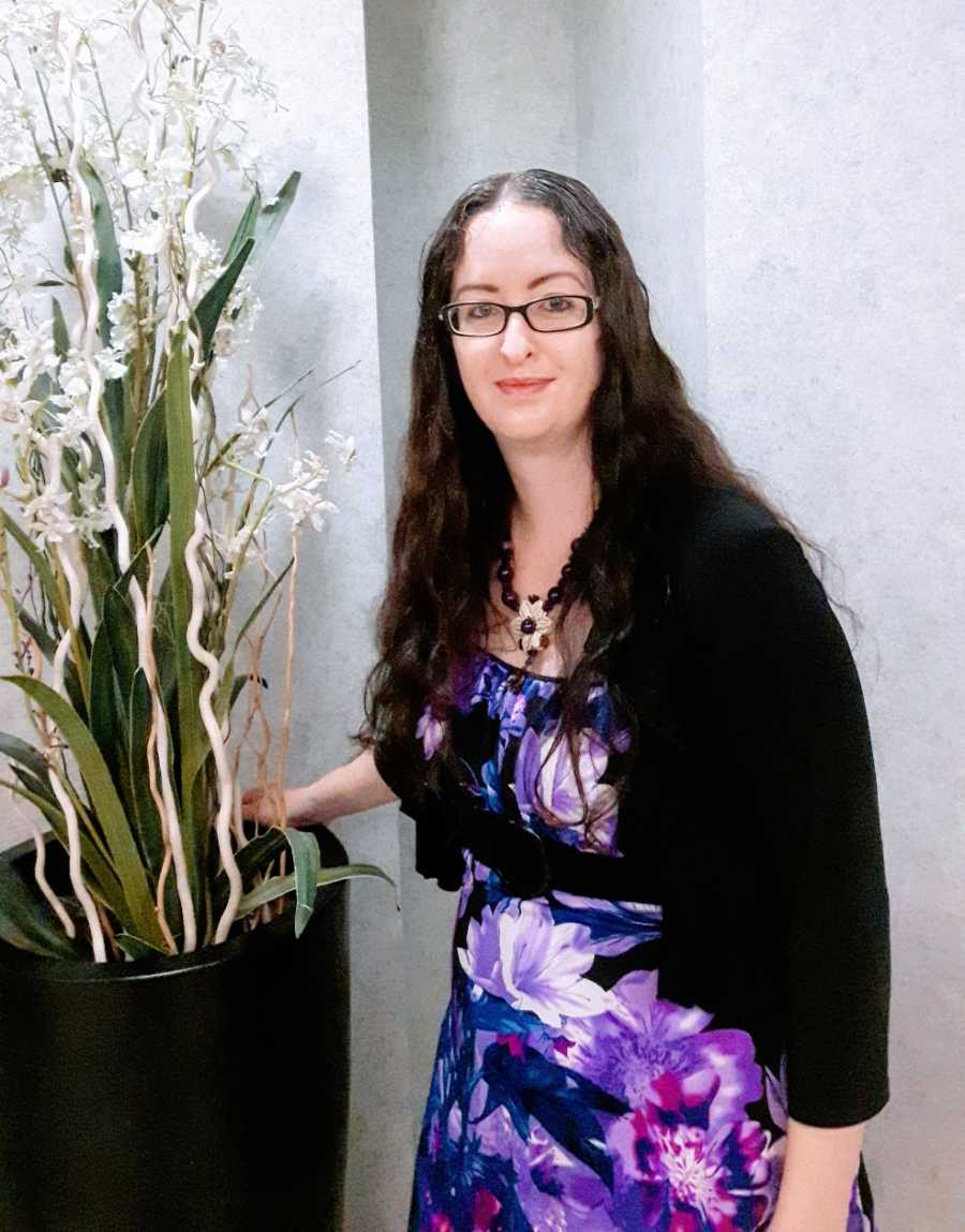 A woman wearing a purple dress stands in an office