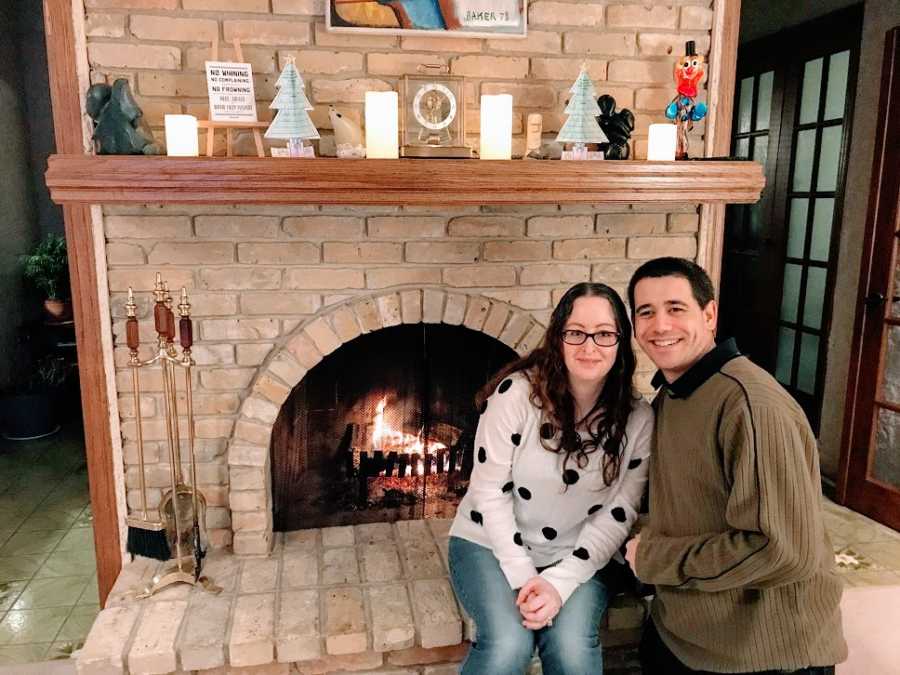 A woman sits with her partner at a fireplace