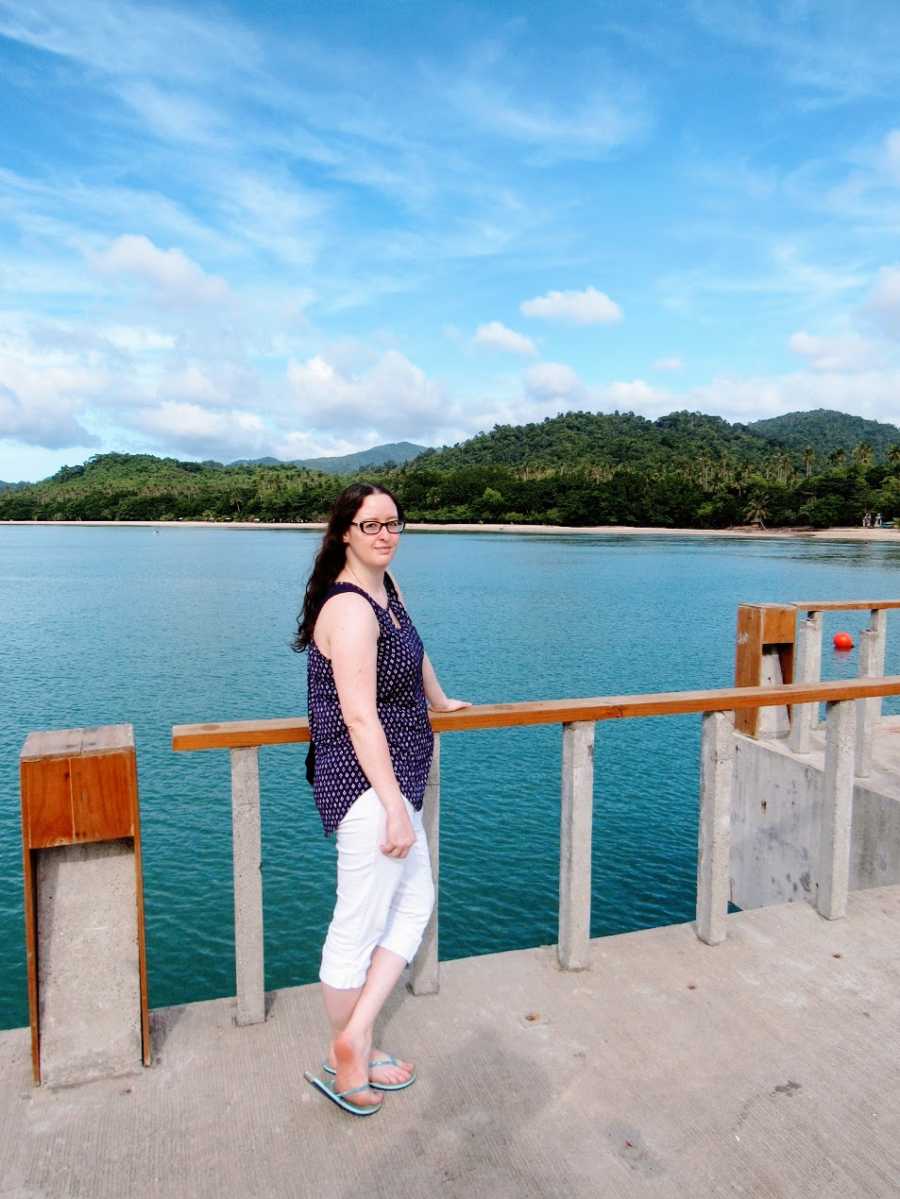 A woman stands by a railing near the water