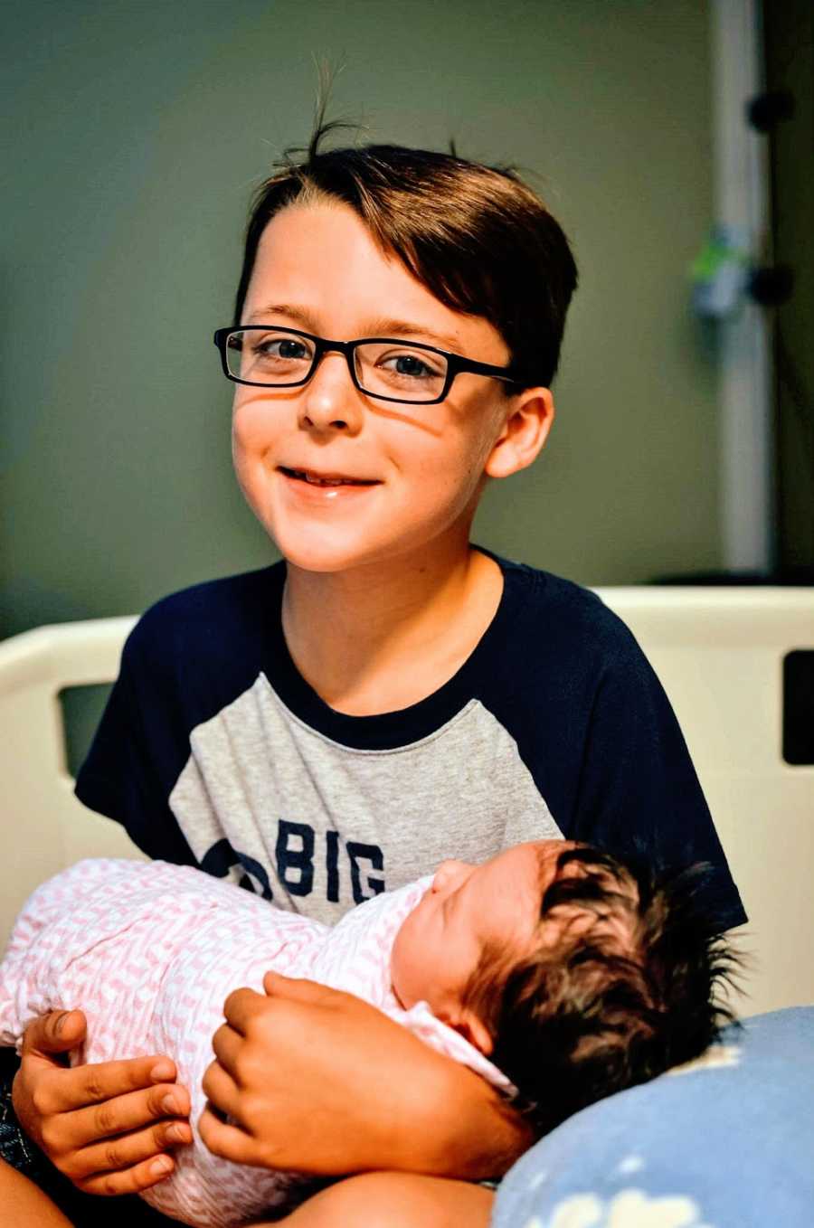 A little boy holds his newborn sister in the hospital