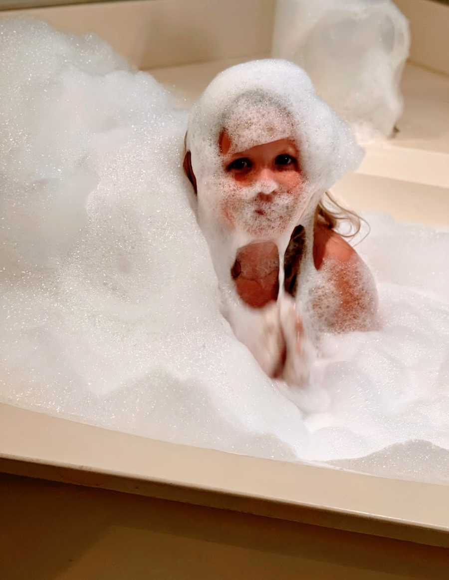 A little girl sits in an overfilled bubble bath