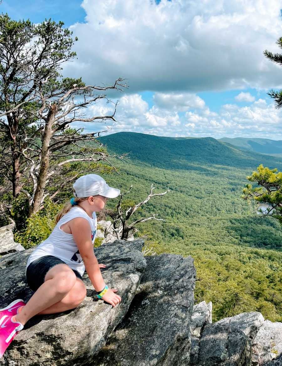 A little girl sits on a rock overlooking a valley