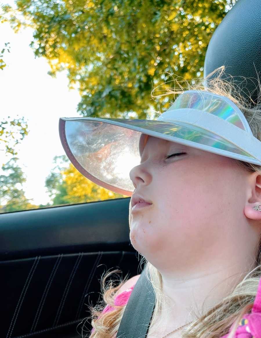 A little girl sleeps in a car while wearing a visor