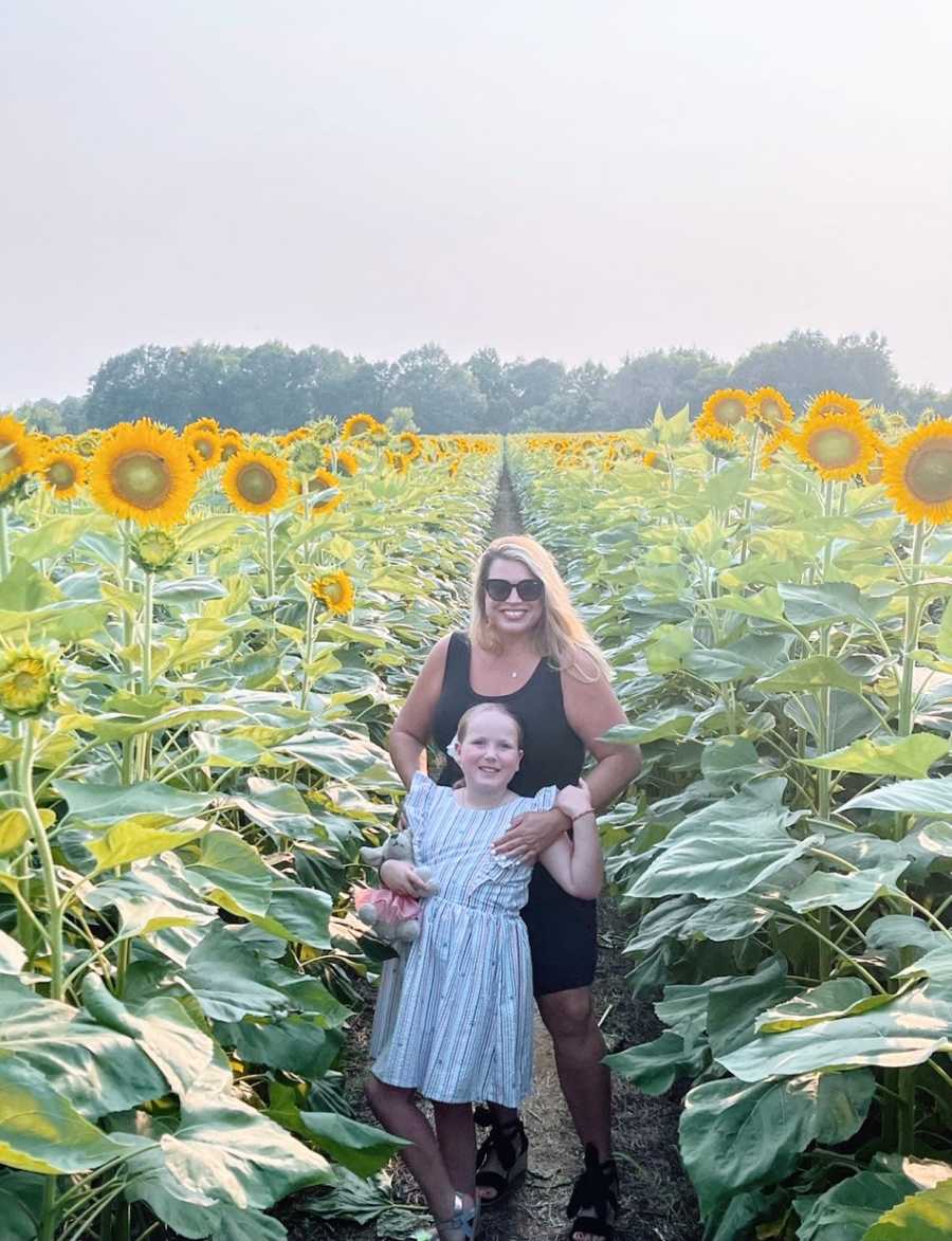 A mother and her daughter stand in a field of sunflowers