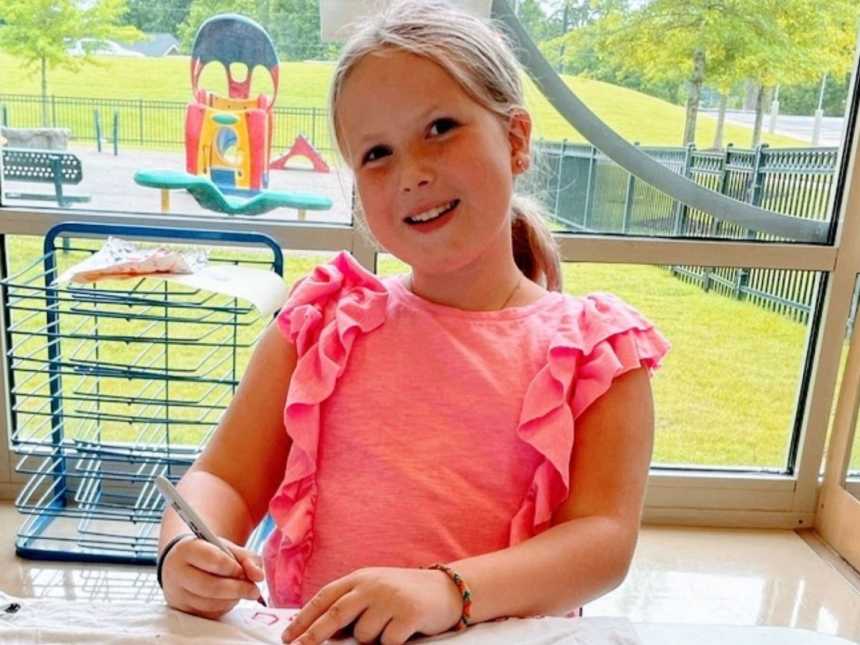 一个穿着粉红色衬衫的年轻女孩坐在桌子旁
