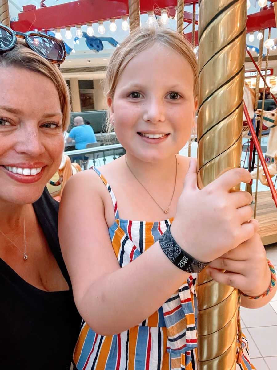 A woman and her daughter stand together on a carousel