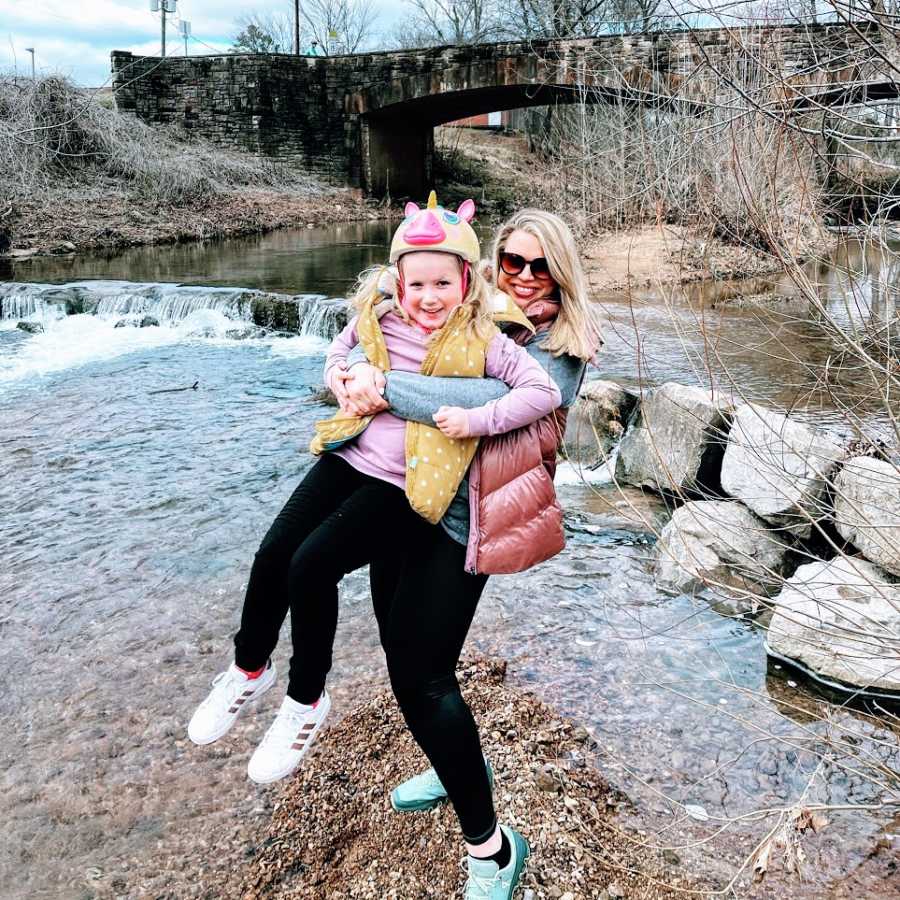 A woman holds her daughter by the water