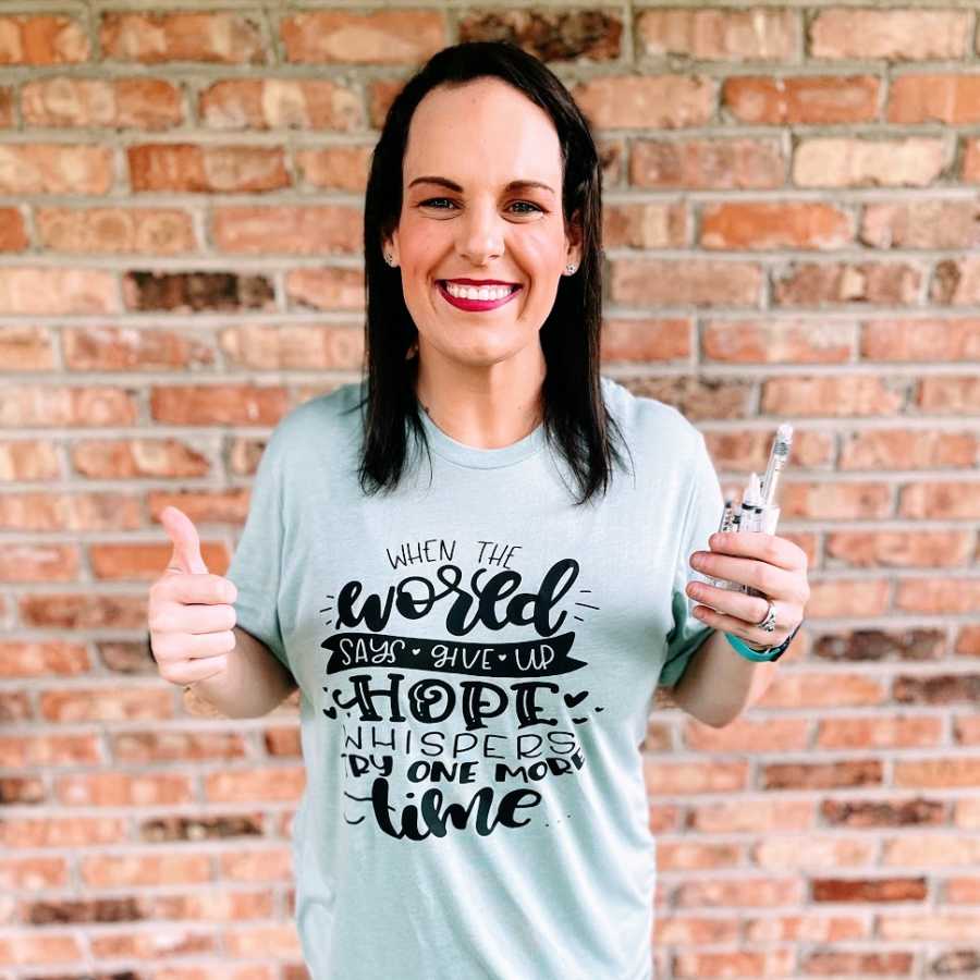 A woman holding a handful of syringes gives a thumbs up