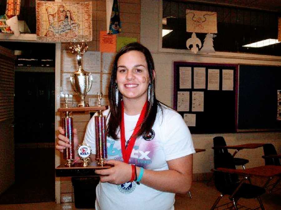 A girl holds up a trophy and wears a medal around her neck