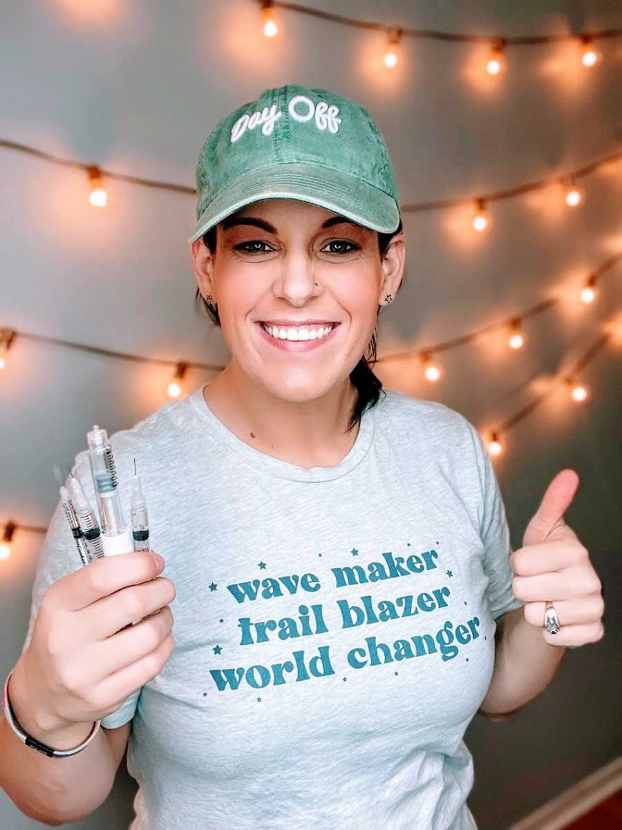 A woman stands holding a handful of syringes