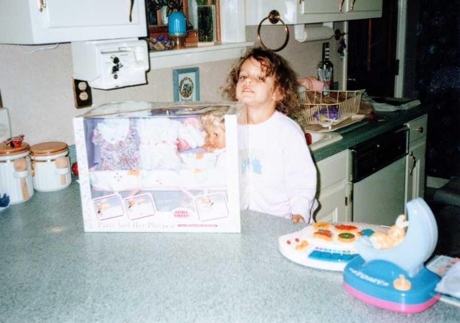 A little girl stands with a box with a doll in it