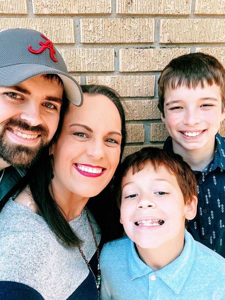 Parents and their two sons stand in front of a brick wall