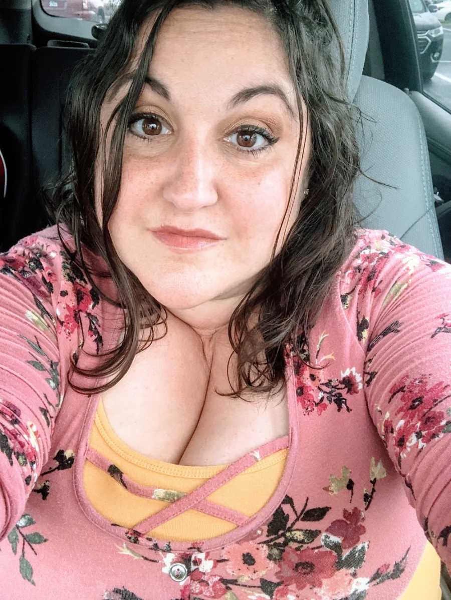 A mom sitting in her car wearing a pink shirt