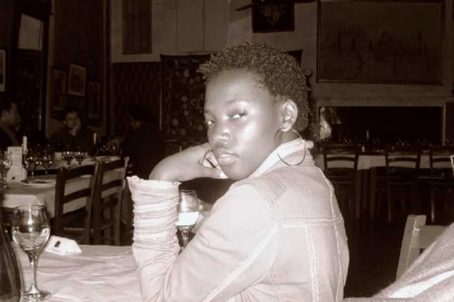 A young woman sits at a table holding a wine glass