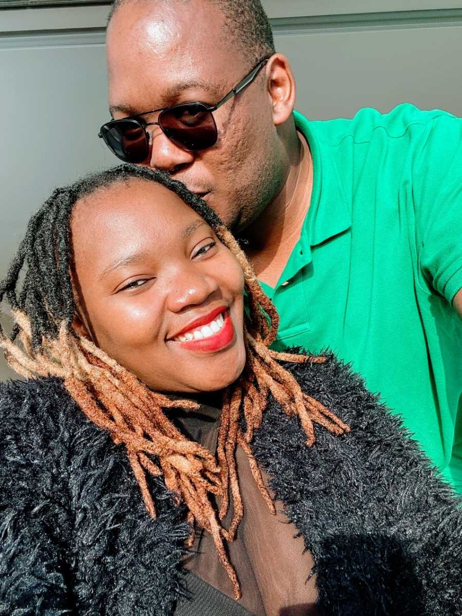 A man wearing sunglasses and a green shirt kisses his wife on the head