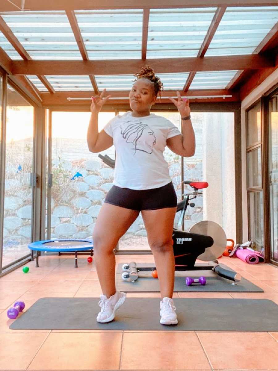 A woman stands in her home gym making peace signs