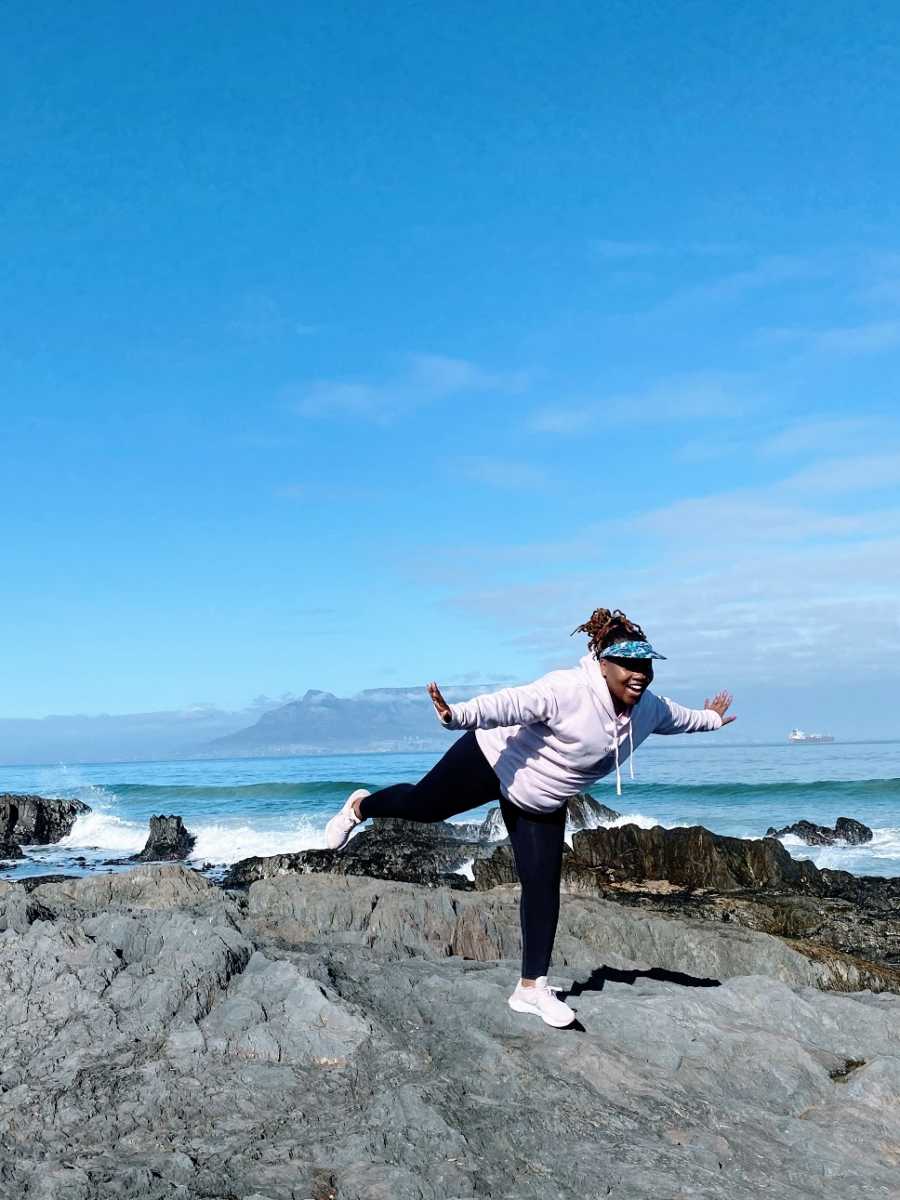 A woman balances on one foot by the ocean