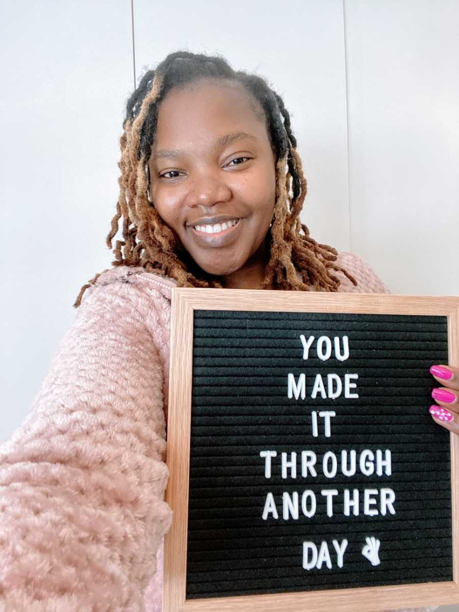 A woman holds up a sign that says "You made it through another day"