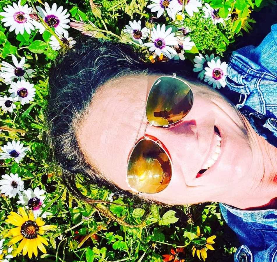 A woman lies in the grass on her back wearing sunglasses