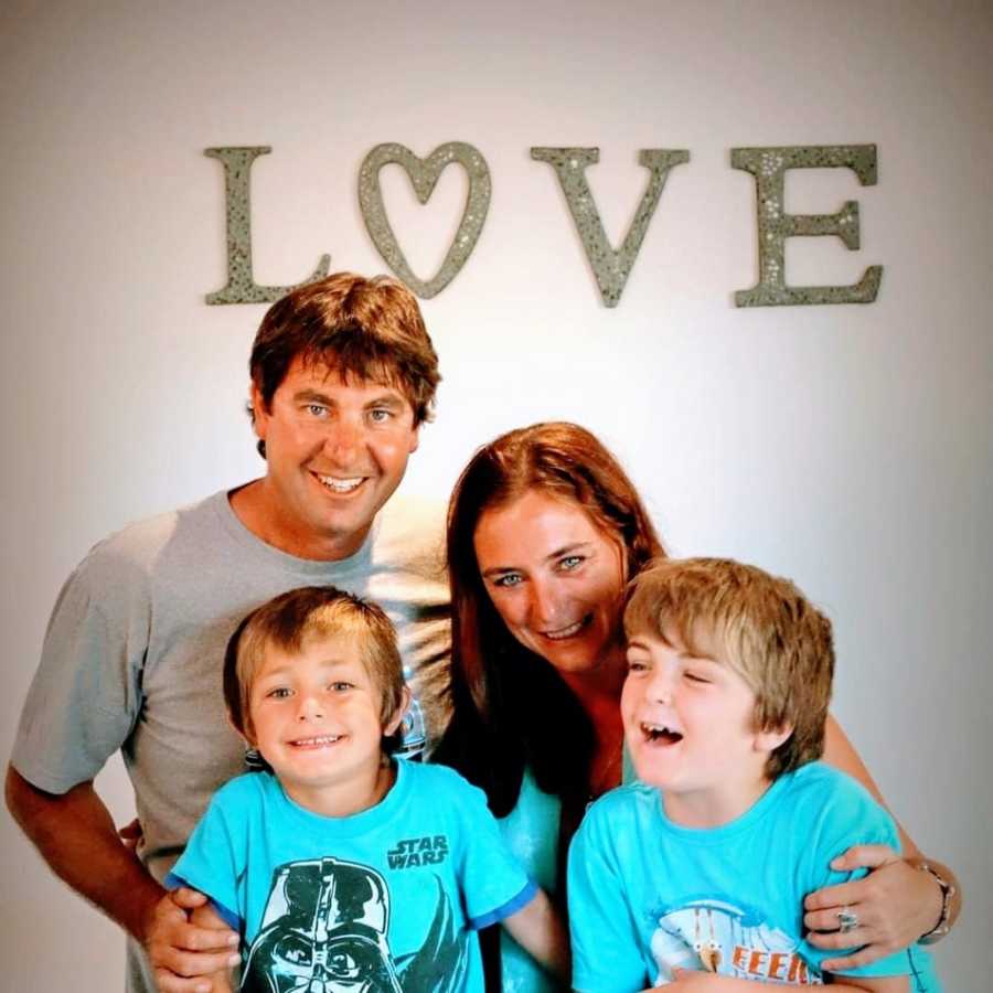 Parents stand with their two children in front of a sign that says love