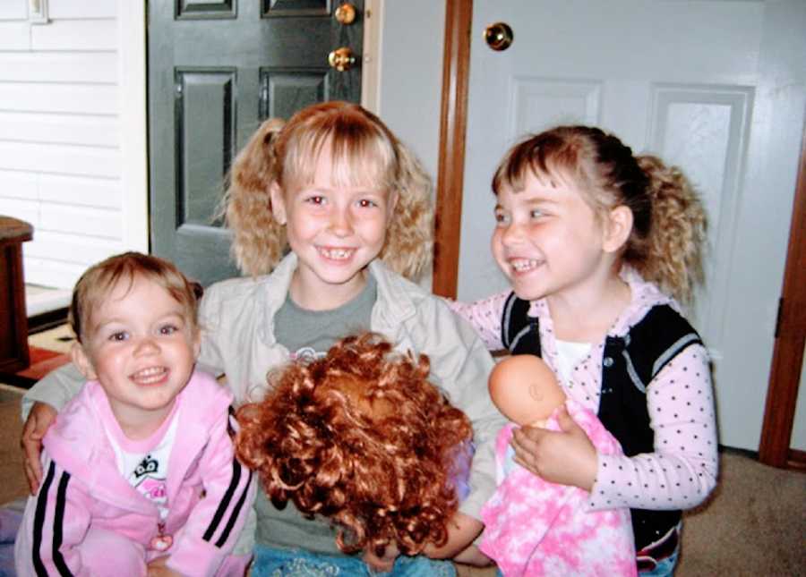 Three sisters sit together with a doll