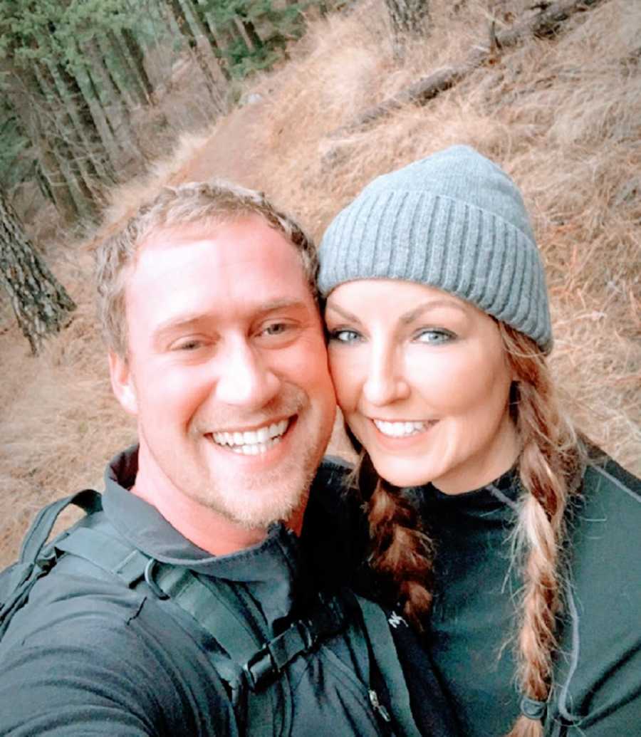 A woman and her husband stand together in the woods