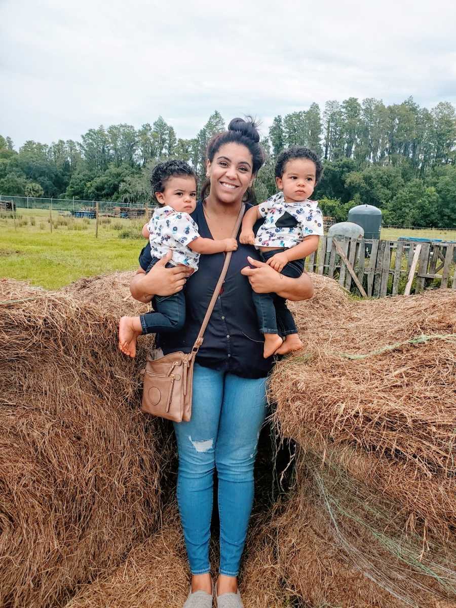 A mom holds her twin sons by a haystack