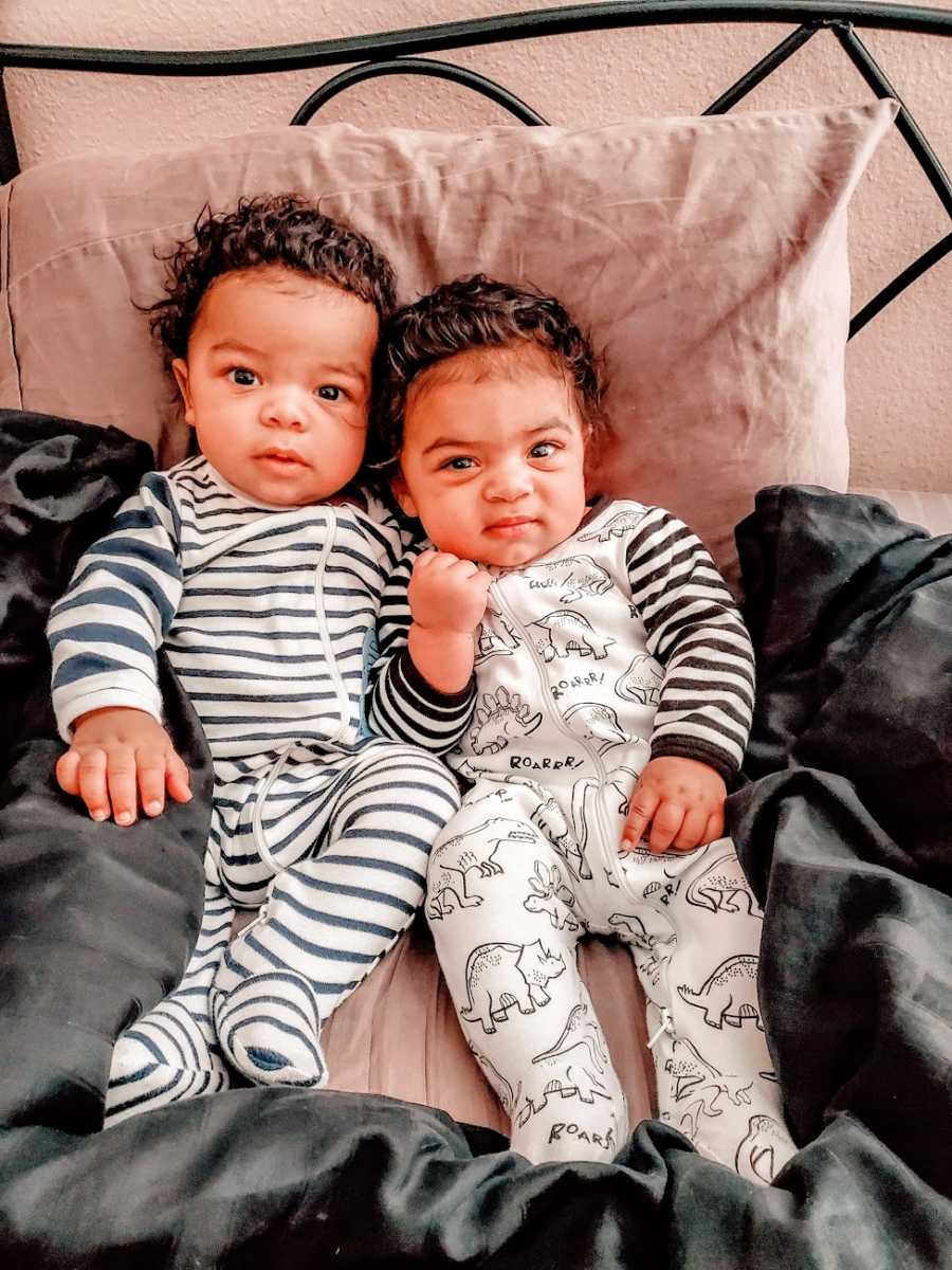 Twin brothers sit next to each other on a bed