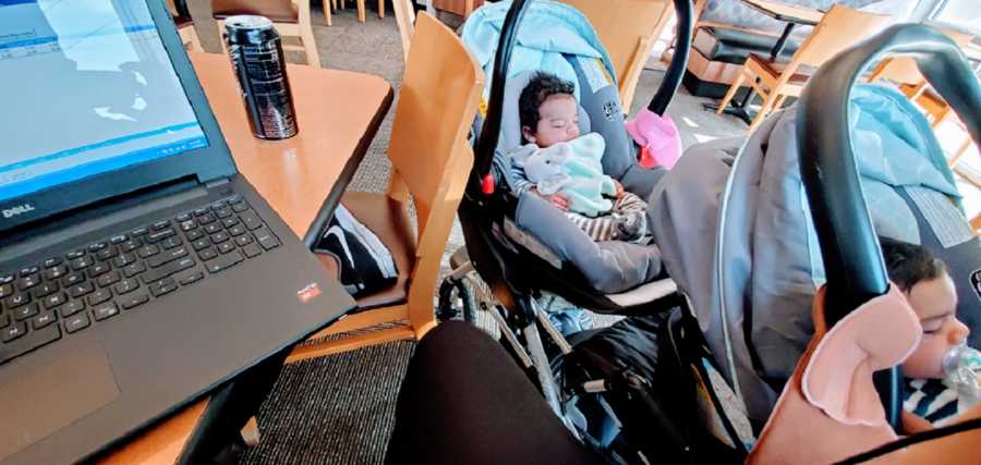 A pair of twins sleep in a stroller next to their mom's computer