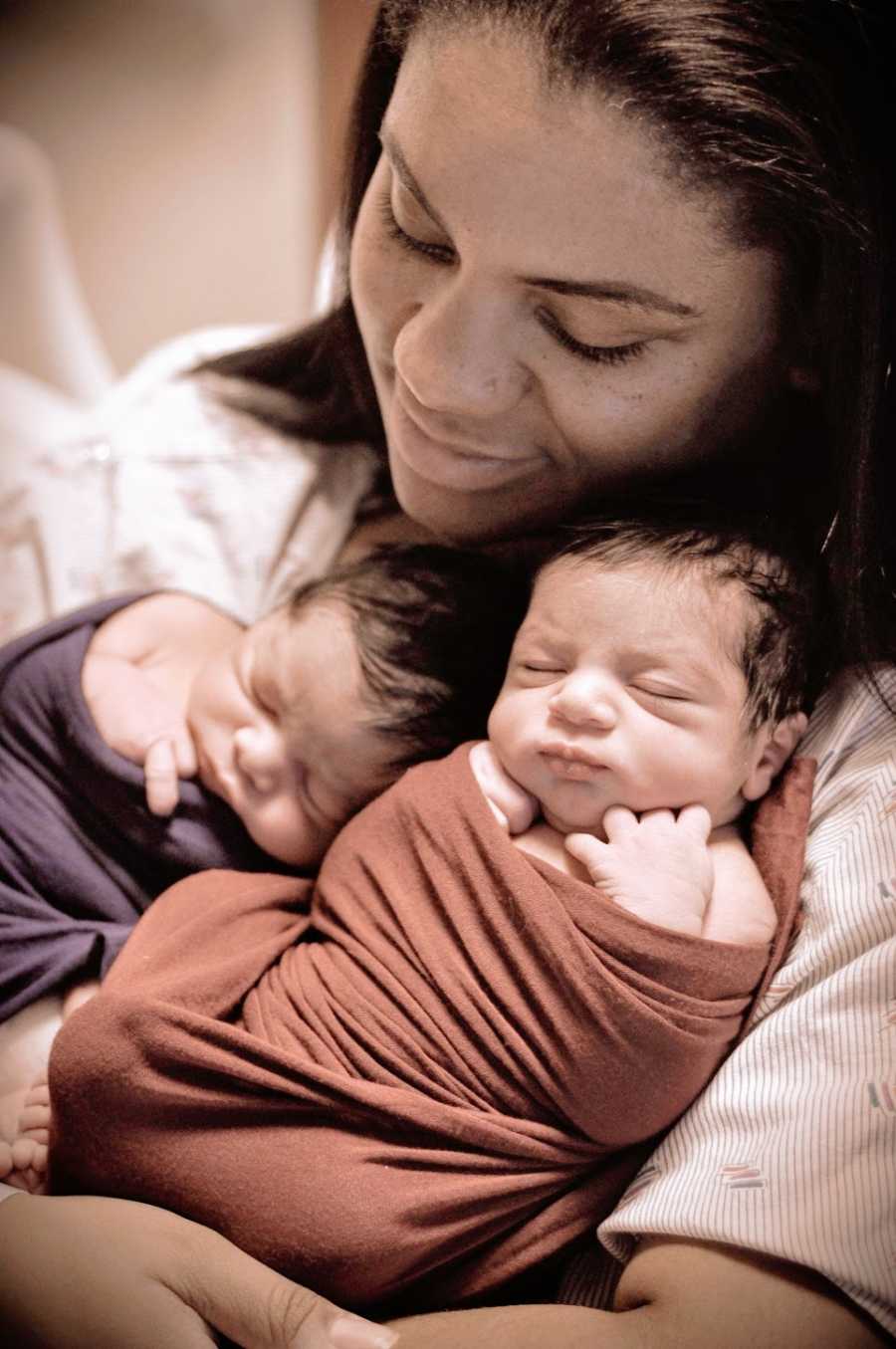 A mother holds her two newborn babies on her chest