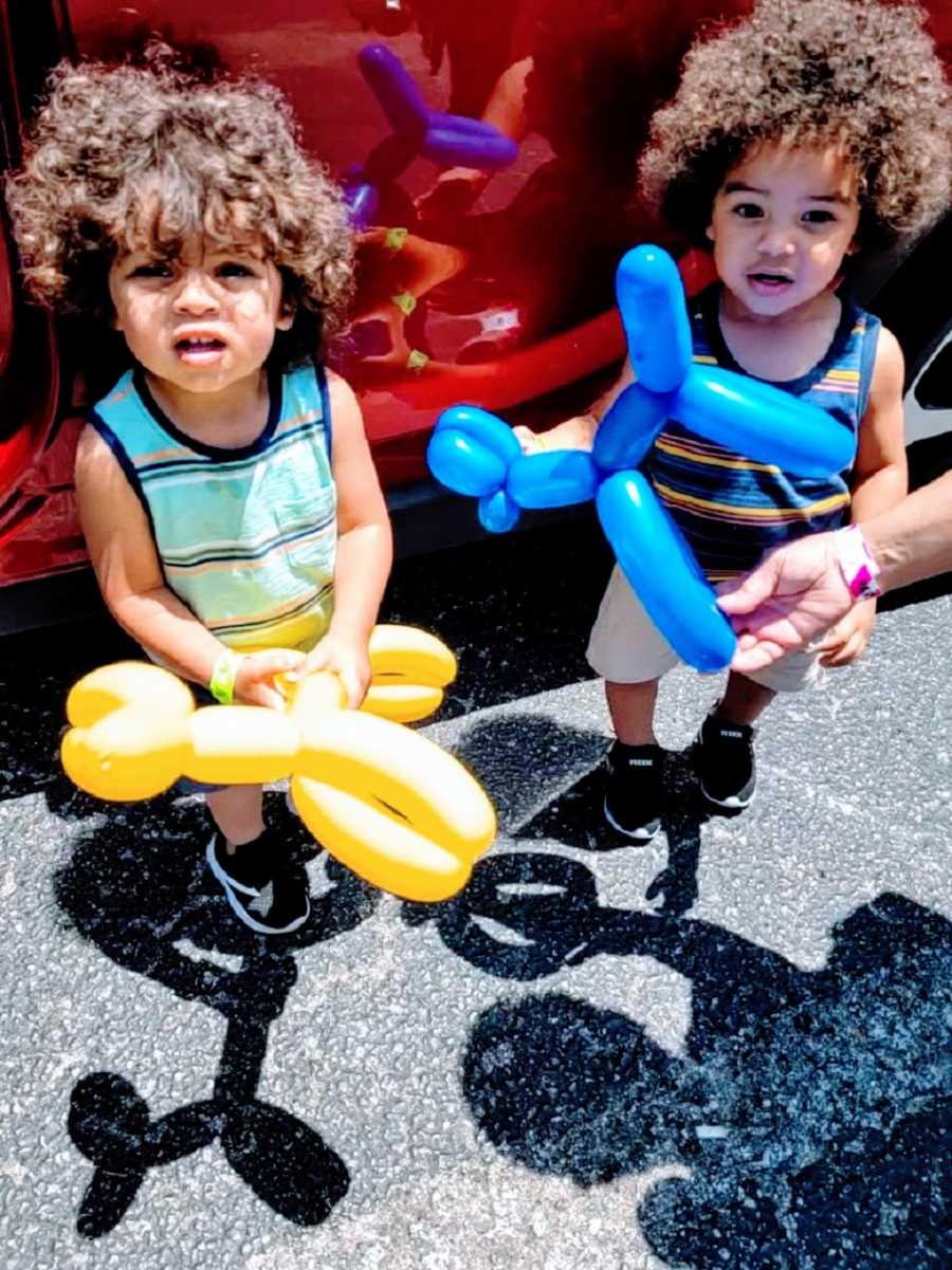 Twin boys stand holding balloon animals