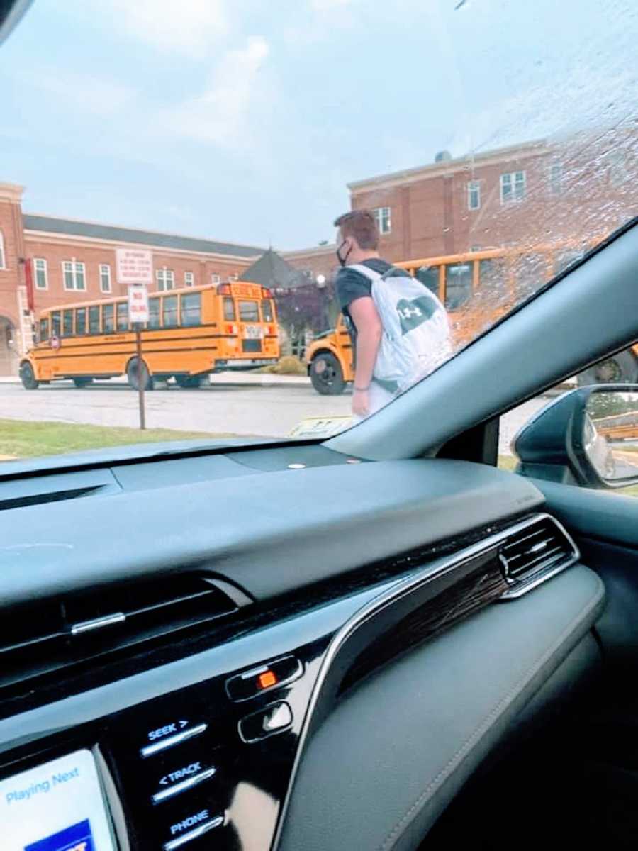 A boy returns to school wearing a mask as seen through a car window