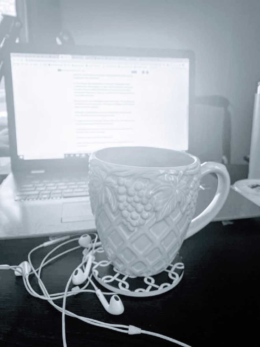 A mug and headphones sit on a desk in front of a computer