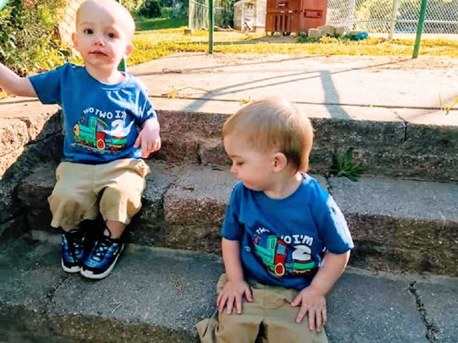 Twin boys wearing matching outfits sitting on steps